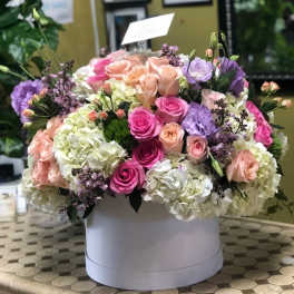 Round box arrangement of pink, peach, white, and lavender flowers