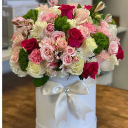 Round hatbox arrangement of pink and white roses with hot pink accents and green dianthus in a white box with satin bow