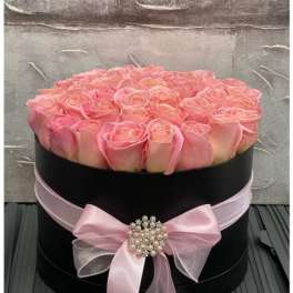 Round black hat box filled with pink roses and tied with a pink bow and pearl brooch.