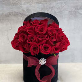 Red roses arranged in a black hatbox with a burgundy ribbon