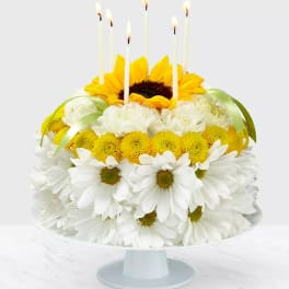 Sunflower and white daisy cake with lit candles on a pedestal stand