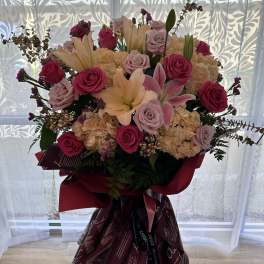 Large bouquet of pink roses, lilies, and hydrangeas in burgundy wrap
