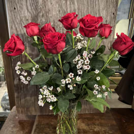 Red roses with small white filler flowers in a clear glass vase