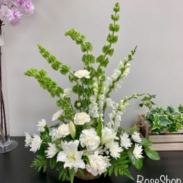 White lilies and daisies in a low basket arrangement with tall green spikes