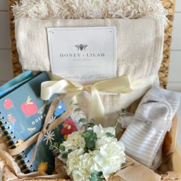 Gift basket with a white throw, notebook, and small white flower bouquet