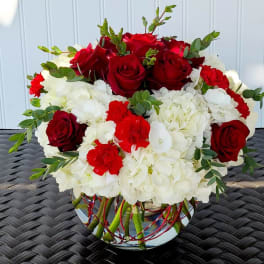 Red roses and white hydrangeas in a glass vase with greenery