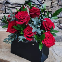 Black gift bag filled with red roses and greenery