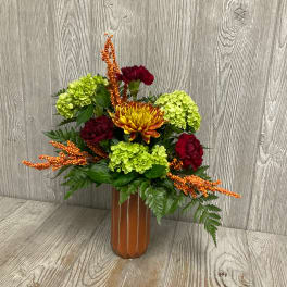 Mixed floral arrangement in a tall orange vase with green and red blooms
