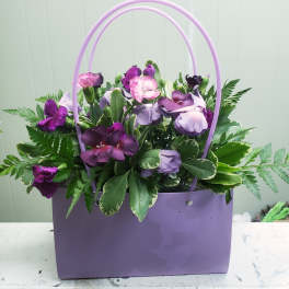 Purple and lavender flowers in a lavender handbag-style container with double handles