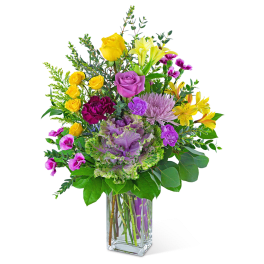 Mixed bouquet of yellow, purple, and pink flowers in a clear glass vase