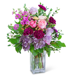 Pink and lavender roses with purple carnations in a clear glass vase