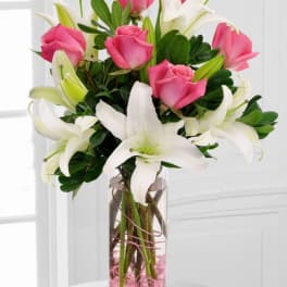 Tall glass vase with pink roses and white lilies accented with pink stones