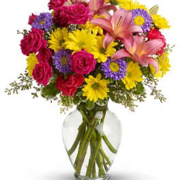 Bouquet of pink roses, lilies, and yellow daisies in a clear glass vase