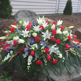 Large funeral spray with white lilies, red roses, and blue flowers