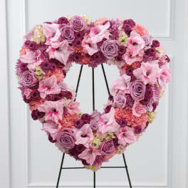Heart-shaped floral wreath in pink and purple tones on a black stand