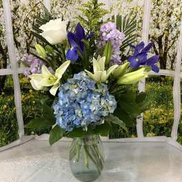 Bouquet of blue hydrangeas, white lilies, and purple flowers in a glass vase