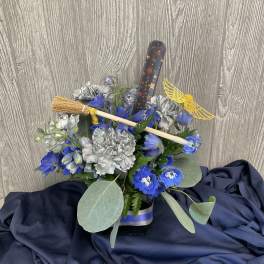 Blue and silver floral arrangement with a broom and winged wand decoration