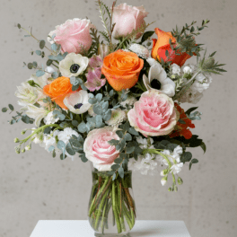 Mixed bouquet of pink and orange roses with white anemones in a clear glass vase