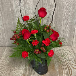 Red roses and carnations arranged in a black skull vase