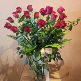 Tall bouquet of red roses in a clear glass vase with a ribbon