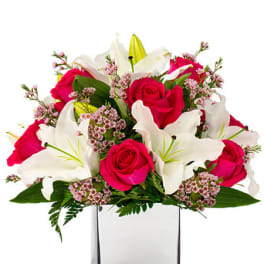 Arrangement of hot pink roses and white lilies in a clear glass cube vase