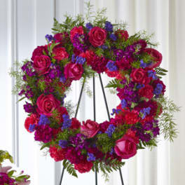 Heart-shaped floral wreath with pink roses and purple flowers on a stand