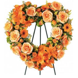 Heart-shaped floral wreath with orange roses and lilies on a stand