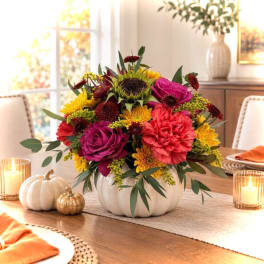 Colorful floral arrangement in a white pumpkin-shaped vase on a dining table