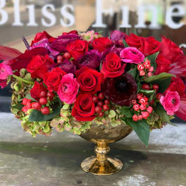 Red and pink rose arrangement in a gold pedestal vase