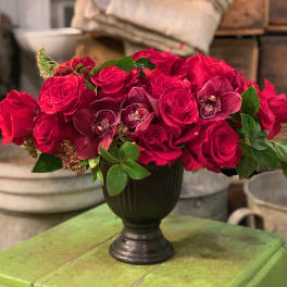 Red rose arrangement with orchids in a dark vase