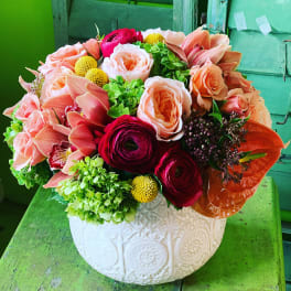 Mixed bouquet of peach, pink, and red flowers in a white ceramic vase