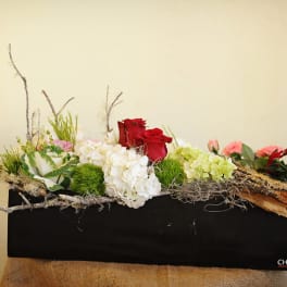 Low floral arrangement with red roses, white hydrangeas, and pink blooms in a black container