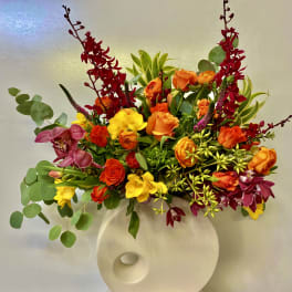 Bright mixed flower arrangement in a white vase with red, orange, yellow, and purple blooms.