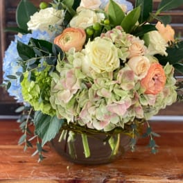 Mixed bouquet of pastel roses, hydrangeas, and ranunculus in a glass vase