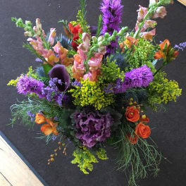 Tall mixed arrangement with purple, yellow, and orange flowers including snapdragons and roses