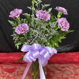 Lavender carnations in a glass vase with a purple ribbon