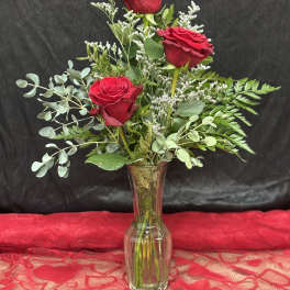 Three red roses in a clear glass vase with mixed greenery