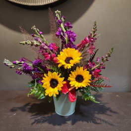 Bright mixed bouquet with yellow sunflowers in a pale vase