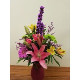 Mixed bouquet with pink lilies, yellow alstroemeria, and purple flowers in a vase