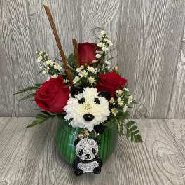 Red roses and white flowers in a green glass vase with a panda charm.