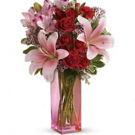 Pink lilies and red roses in a tall pink glass vase