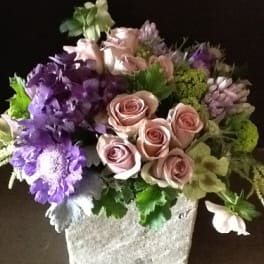 Mixed bouquet of pink roses and purple flowers in a square stone vase