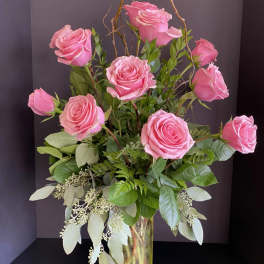 Pink roses arranged in a clear glass vase with mixed greenery