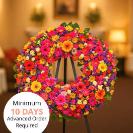 Bright circular standing wreath of mixed pink, orange, yellow, and purple flowers on a black easel indoors