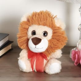 Plush lion toy with a red ribbon bow sitting on a table