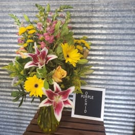 Mixed bouquet with yellow daisies, pink lilies, and roses in a glass vase