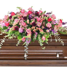 Pink and purple mixed flower casket spray in a lush, cascading style on a wooden casket