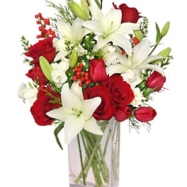 Tall clear vase with white lilies, red roses, and red berries in a mixed arrangement
