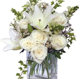 White lilies and roses arranged with accent blooms in a clear rectangular glass vase