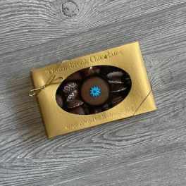 Gold box of assorted chocolates with a clear window showing a round piece topped with a blue flower design